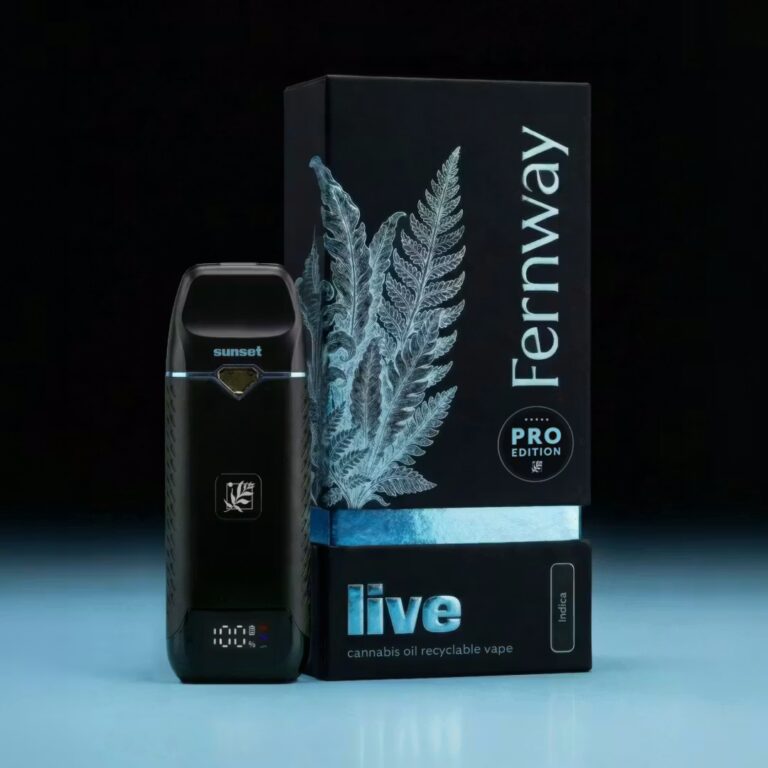 Fernway Live Cannabis Oil Recyclable Vape – Purple Sunset Product photo of the Fernway Pro Edition Live Cannabis Oil Recyclable Vape in the Purple Sunset strain (Indica), displayed against a dark background with cool blue ambient lighting. The sleek black vape device features a small digital display showing 100% battery and a blue accent ring, with the strain name "sunset" printed near the top. It is positioned in front of its premium black and blue packaging, which is embossed with a detailed fern illustration and labeled "Fernway Pro Edition – Live Cannabis Oil Recyclable Vape – Indica."